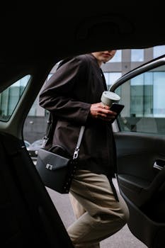 Stylish woman entering a car, holding coffee and smartphone, showcasing urban lifestyle.